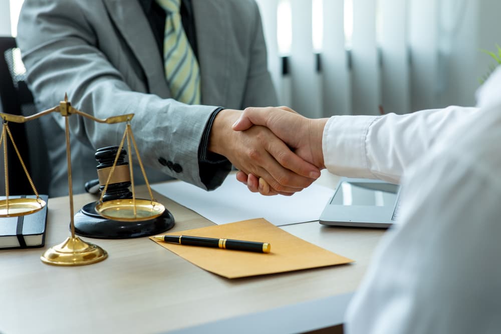 Close-up image of lawyer and client shaking hands on a table, symbolizing the concept of justice and law.