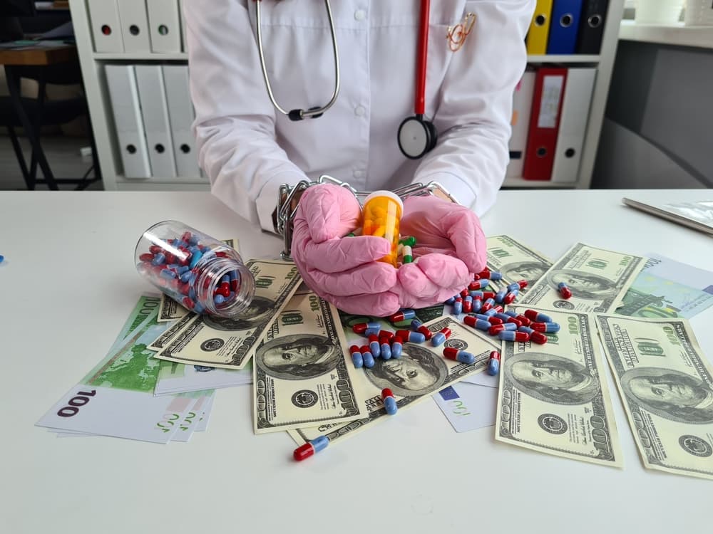 A hand holding pills chained with cash euros and dollars, representing illegal prescription drug sales.