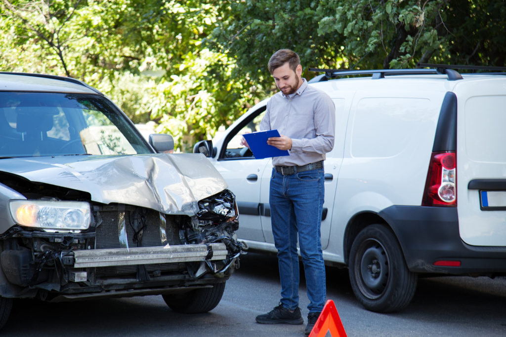 An insurance officer writing on clipboard about the damages after the car accident