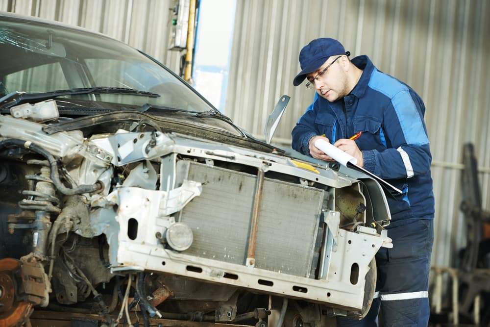 Skilled automotive repair professional inspecting and determining damage on a metal body car in the automotive industry.