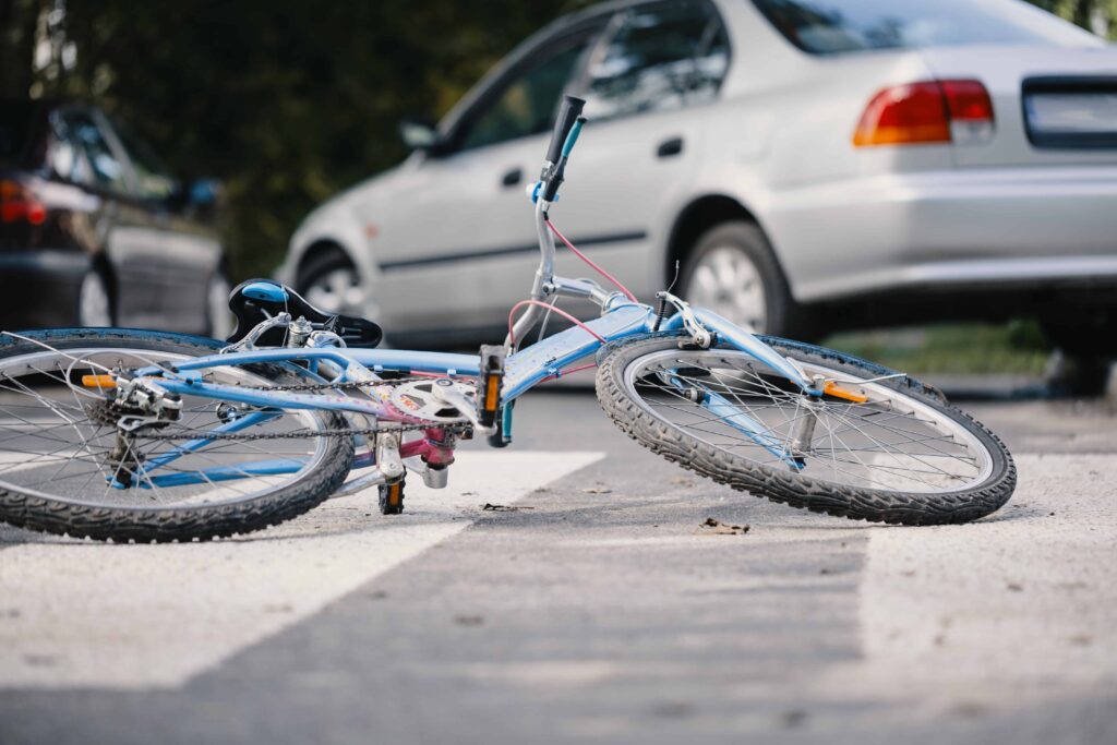 Bicycle lying on the road after a traffic accident, with a car stopped in the background.