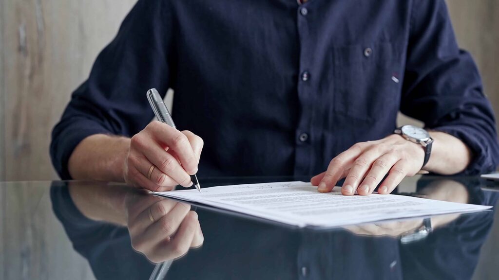 Person signing a legal document at a desk, completing paperwork