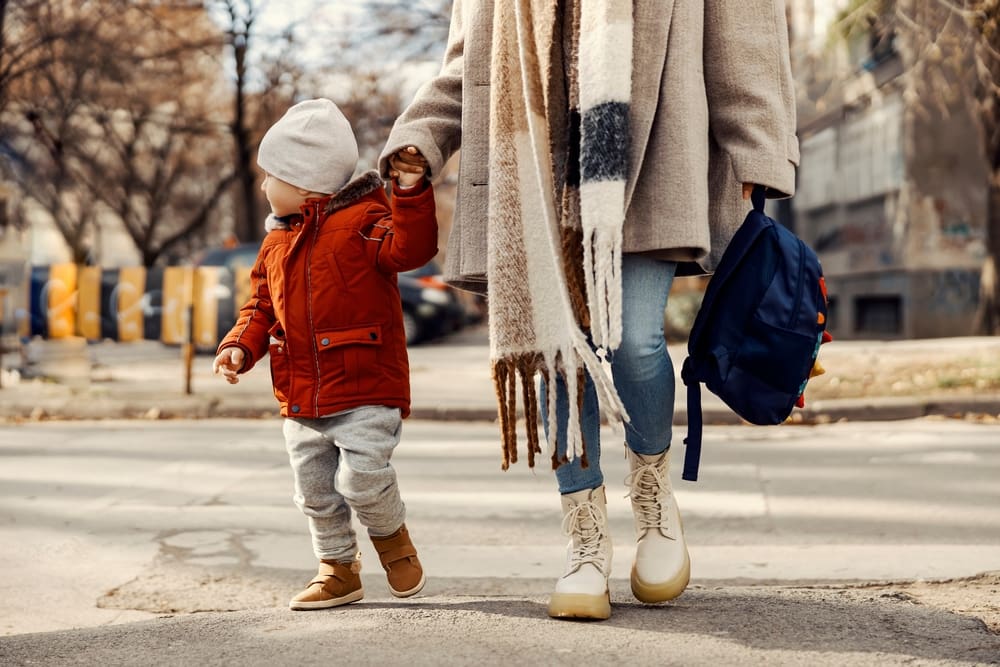 Parent holding a young child’s hand while walking outdoors with a backpack